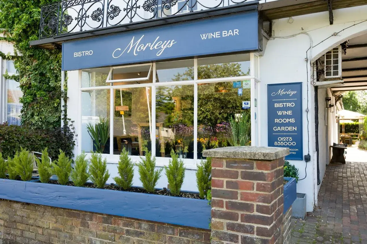 The front of Morleys: a blue sign reading Bistro, Morleys, Wine bar above a wide window with a planter of small trees, and the archway beside it