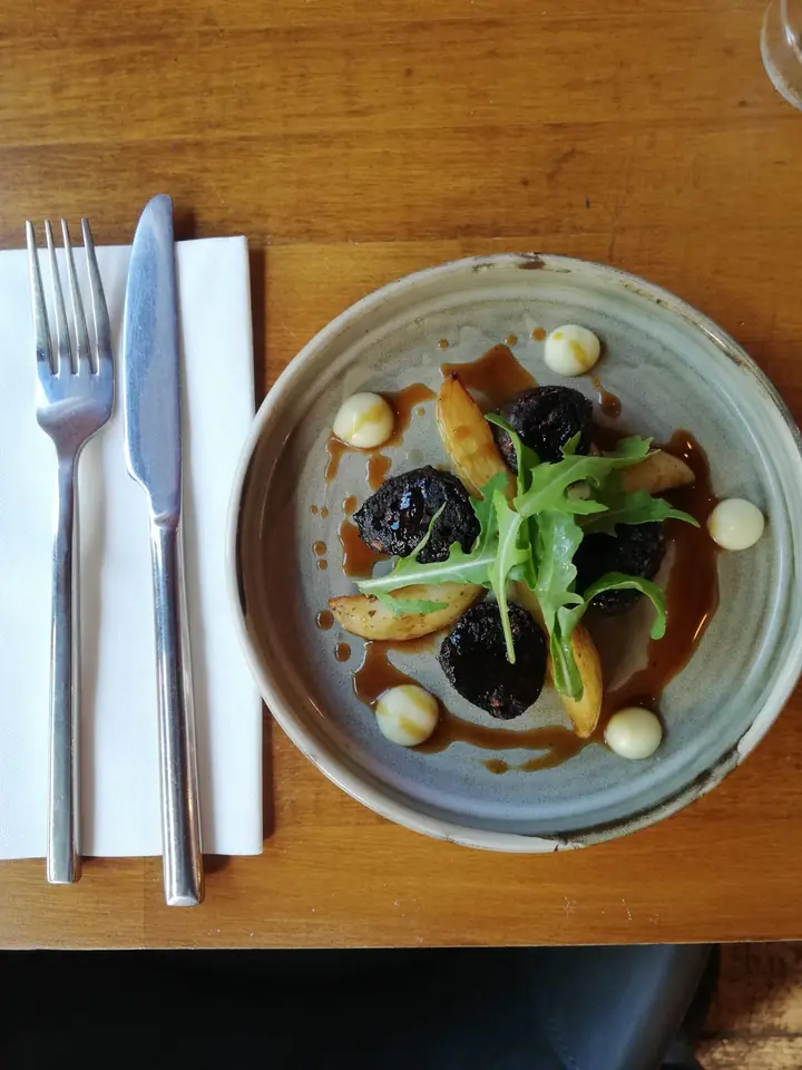 Black pudding with roast potatoes, rocket and a glossy sauce in a stoneware bowl