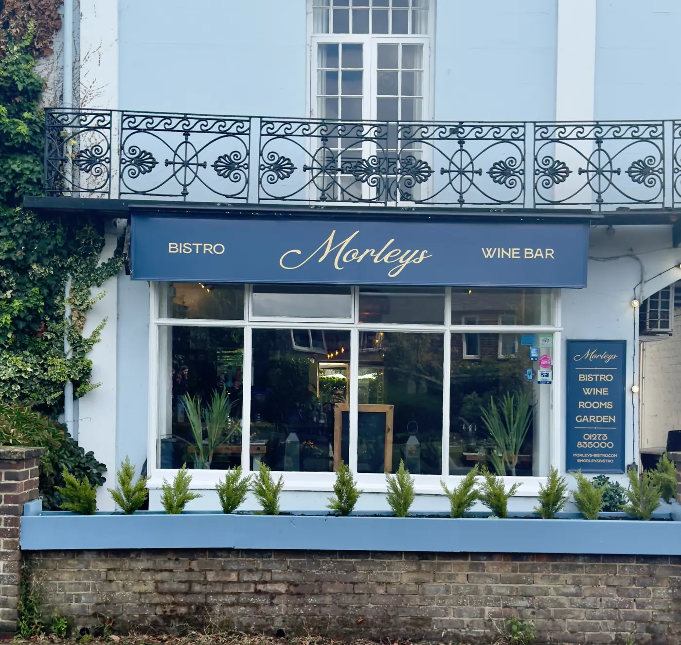 The front of Morleys: a blue sign reading Bistro, Morleys, Wine bar above a wide window with a planter of small trees